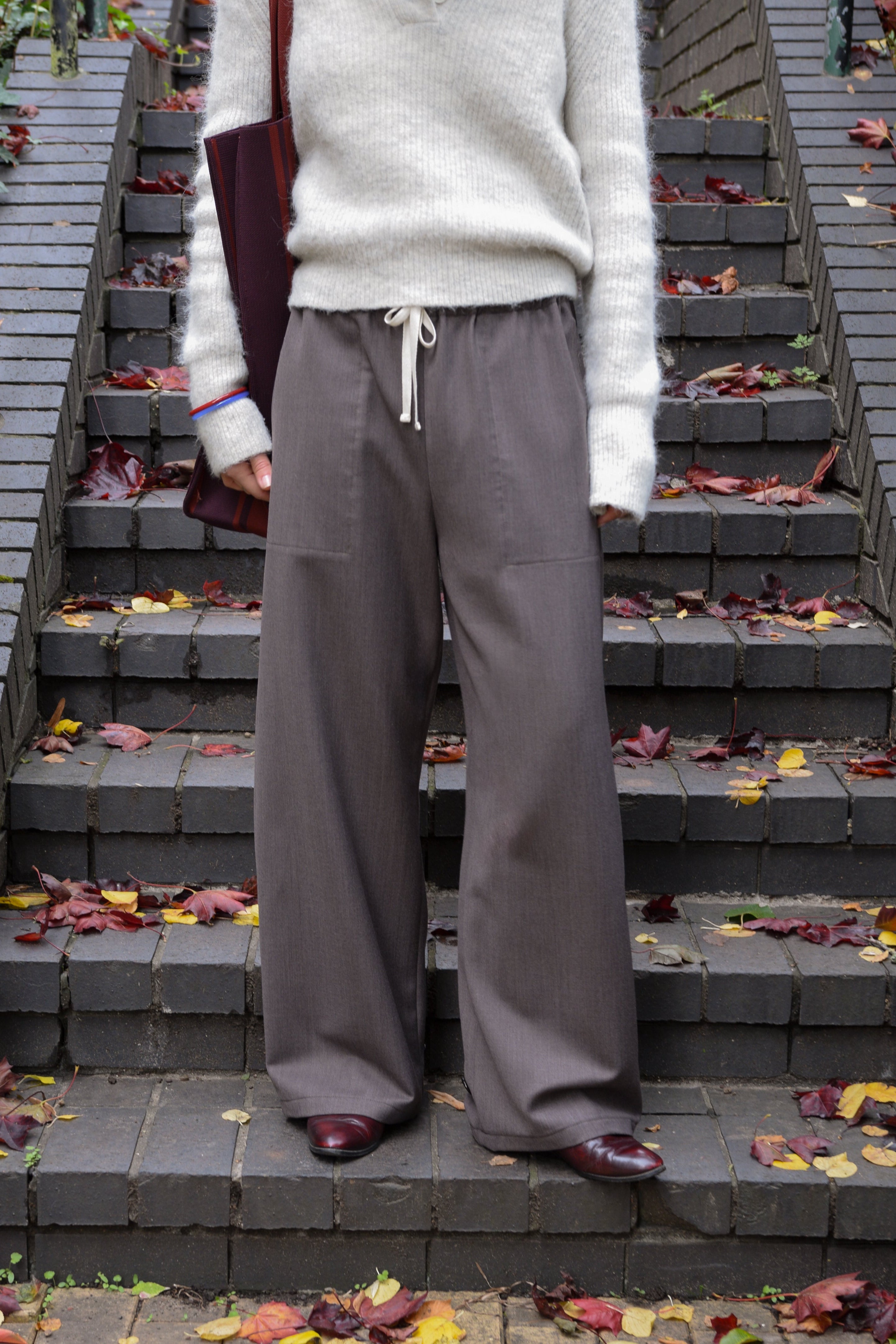 Person wearing a white sweater and gray pants standing on a staircase with autumn leaves.