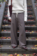 Person wearing a white sweater and gray pants standing on a staircase with autumn leaves.